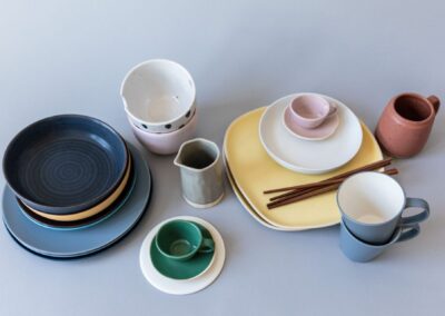 A diverse collection of ceramic tableware including plates, mugs, bowls, and cups on a blue surface.